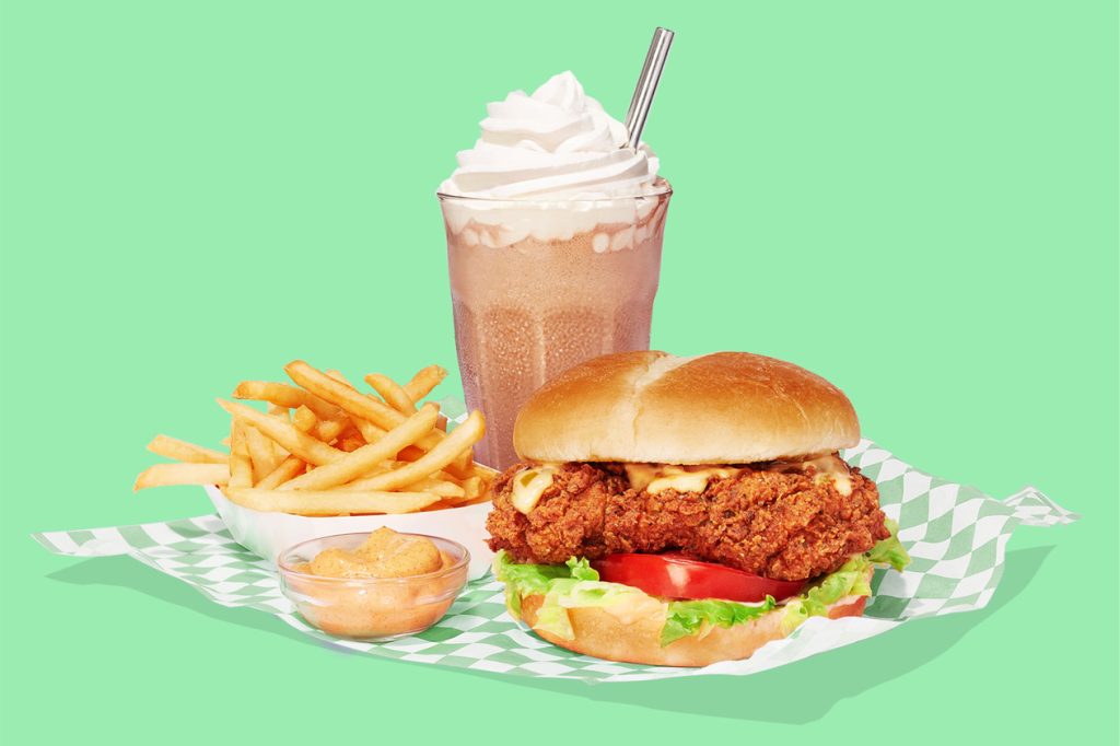 A burger, fries and a milkshake on a green background.